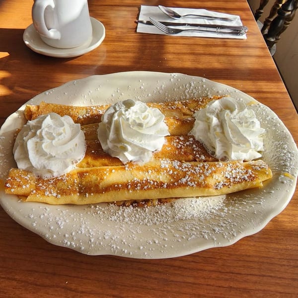 Three golden crepes topped with whipped cream and powdered sugar on a white plate.