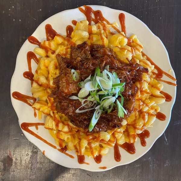 Macaroni and cheese topped with pulled pork, green onions, and a drizzle of BBQ sauce.