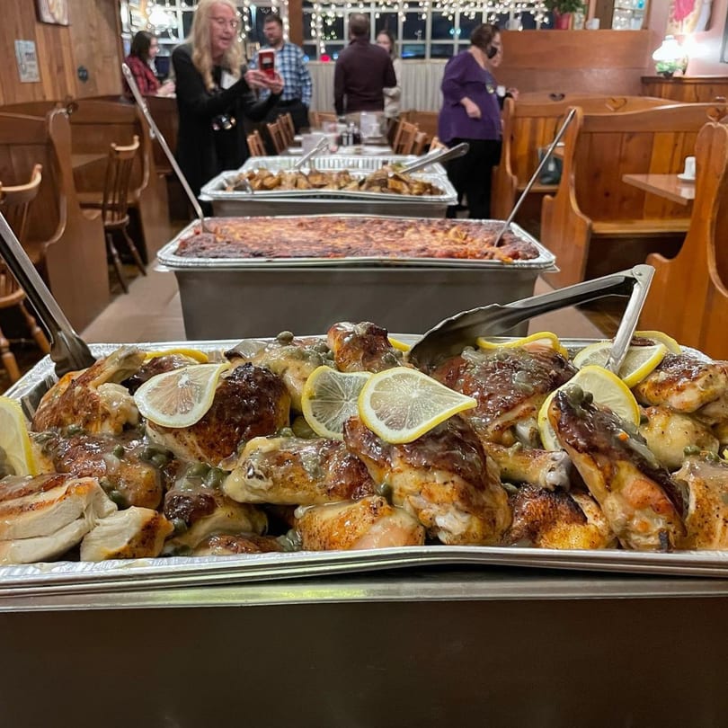 Buffet line with lemon chicken, roasted potatoes, and baked ziti, with guests in the background.