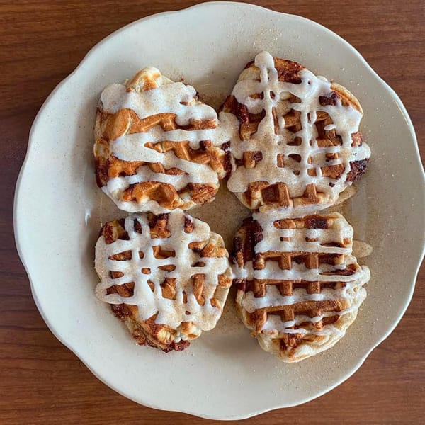 Four cinnamon roll waffles drizzled with white icing on a light-colored plate.