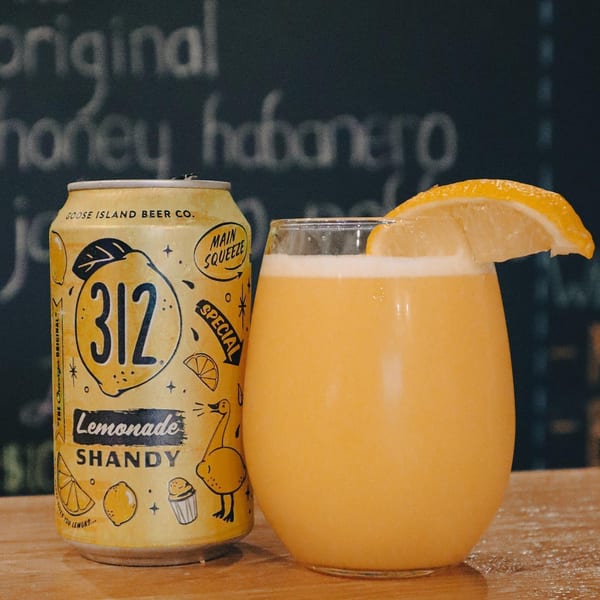 A Goose Island 312 Lemonade Shandy can next to a glass of the drink with a lemon slice.